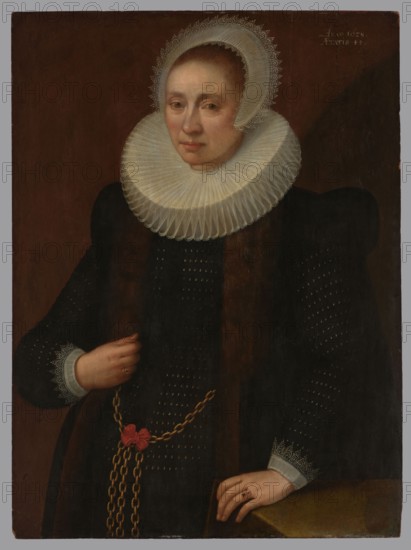 Portrait of a Lady Portrait of a Woman, Geldorp, Melchior fl. 1602–1637 painter, 1628, oil painting; height 88 cm, width 65.5 cm; with frame: height 119 cm, width 96.5 cm, thickness 9 cm., A woman is shown from the waist up against a dark brown background wearing a black dress with puffed shoulders and decorative small light dots; she has pale skin and a composed facial expression. She wears a large white pleated ruff collar and a white lace-trimmed cap framing her hair, with matching lace at her wrist cuffs. Her hands are visible, one resting on a surface and the other holding a long gold chain with a red ribbon tied to it; both hands show rings. The overall colors visible are black, white, brown, gold, red, pale flesh tones, and subtle gray.