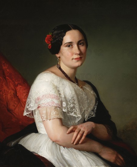 Portrait of Katarzyna Jahn, the artist's sister; Józef Simmler 1823–1868, painter; 1849; oil painting., A seated woman with dark hair styled in a center part and low bun, adorned with red flowers, looks toward the viewer with a neutral expression; she wears a white dress with a sheer, embroidered lace shawl and a dark shawl draped over one shoulder, and she has dangling earrings and a dark beaded necklace. Her hands are folded gently in her lap. The background is a muted green, and there is a visible red patterned fabric on one side. Visible colors include white, dark brown or black, red, green, pink, and flesh tones.