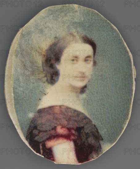 Portrait of Princess Izabella Dzialynska née Czartoryska 1830–1899, daughter of Adam Jerzy and Anna Zofia née Sapieha, founder of the museum at Goluchów castle; artist unknown. Bust in profile right, head three-quarter left; dark hair gathered at the back; wearing a crimson crinoline dress with a black bertha at the neckline and short sleeves. Background grey-blue, lightened around the head. Miniature deformed, 1885, probably France; height 4.8 cm, width 3.8 cm., An oval portrait of a young person with dark brown hair pulled back, pale skin, and a soft, neutral expression, shown from the shoulders up and turned slightly to the side; they wear a dark reddish-brown off-the-shoulder garment with some darker shadowing, and the background is a muted bluish-green; the portrait sits on a pale, slightly worn oval backing with visible texture and edges in beige and off-white.