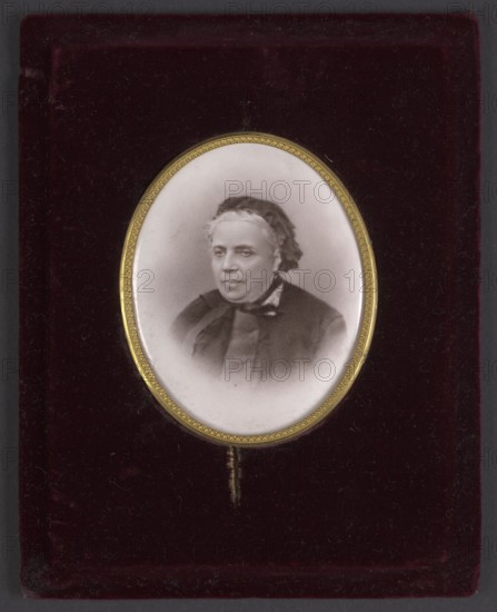 Portrait of Mlle Rousset at about age 70 died 1893, secretary and librarian of Izabella; photographer: Braun, Adolphe 1812–1877 from 1889 Braun, Clément et Cie, and 1910 – Braun e. Inscription notes: Josephine Rousset, niece of the Czartoryski doctor younger than Izabella, a student of the Hotel Lambert, a companion of the Czartoryskis' youth, over time gathered in her hands the administrative threads of Izabella's activities, and partly of Wladyslaw Czartoryski's. Date: 1870, place of creation: France. Medium: miniature. Dimensions: height 6.8 cm, width 5.4 cm. Subjects/attributes: en face portrait, woman, headgear., A small oval framed portrait of an older person with light-colored hair and a dark head covering, shown from the shoulders up, set against a white oval mat and surrounded by a thin decorative gold rim; the portrait rests on a dark burgundy velvet background with visible texture and a narrow dark gray border around the outer edge, and the portrait shows tones of black, whi...