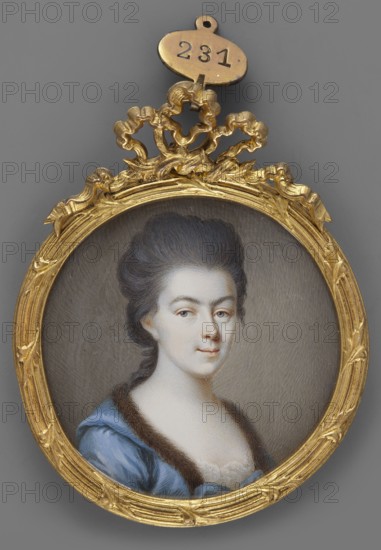 Amalie von Hessen-Darmstadt Margravine von Baden 1754–1832; artist: Hill, Friedrich Jakob 1785–1846, painter. Subject: female portrait, 3/4 bust right, young woman, grey eyes, dark grey wig with a long strand of hair at the nape, exposed forehead. Costume: blue dress trimmed at the neckline with brown fur; hairstyle noted. Style/type: miniature; foreign miniatures. Inscriptions/notes: binding gilt bronze, bow-shaped finial. Date/place: 1785, Germany. Dimensions: height 5.4 cm, width 5.2 cm., An oval portrait set in an ornate gold frame with decorative bow-like ornament at the top, showing a woman with pale skin and dark hair styled high and swept back, wearing a blue garment with a dark fur trim and a hint of white lace at the neckline, against a muted gray background; visible colors include gold, pale skin tones, dark brown, blue, white, and gray.