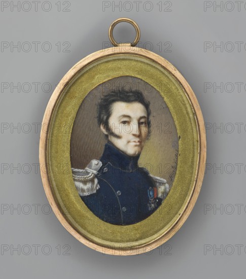 Portrait of a senior officer of the army of the Kingdom of Poland with the Order of Virtuti Militari and the Legion of Honour, traditional title: Kazimierz Lux 1780–1846. Painter: Jedrzej Józef Hintz fl. 1807–1842. Portrait en trois-quarts; miniature height 4.9 cm, width 3.8 cm. Subject: young military man, bust 3/4 right; black, short, slightly disheveled hair, slanting sideburns. Navy blue uniform with silver piping, buttons and axles. Two orders visible: Virtuti Militari and the Legion of Honour. Background: brown-gray on the left, off-yellow on the right. Binding: narrow gilded iron rim, beveled glass, hanging ring. Poland; dated 1817., An oval painted portrait set in a circular metal frame with a round hanging loop, showing a man from the chest up wearing a dark blue military coat with light-colored decorative shoulder pieces and a small medal, the man has dark hair, sideburns, and a pale face with a neutral expression, the painted background behind him is muted brown and olive to...