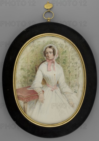Mathilde Karoline Wilhelmine von Bayern 1813–1862, daughter of Ludwig I of Bavaria; portrait knee-length, torso turned right, head three-quarters left with her right hand resting on a brown table upholstered with light cherry fabric. Blond hair, hazel eyes, white bonnet trimmed with pink bows. White dress with a pink ribbon at the waist, gold chain attached to the bodice, gold bracelet on the right hand. Background: trellis entwined with ivy vine. Frame: narrow profiled gilded bronze on polished and black-painted wood. Miniature, 1848, Germany. Height 16.5 cm, width 12.6 cm., An oval framed portrait showing a seated woman wearing a white dress with a pink ribbon at her neck and a matching pink sash at her waist, a white lace bonnet framing her brown hair, and a delicate pale complexion; she rests one hand on a red cushioned stool and the other on her skirt, with a background of pale green leafy vines and a light architectural trellis; the frame is black with a gold inner rim and a smal...