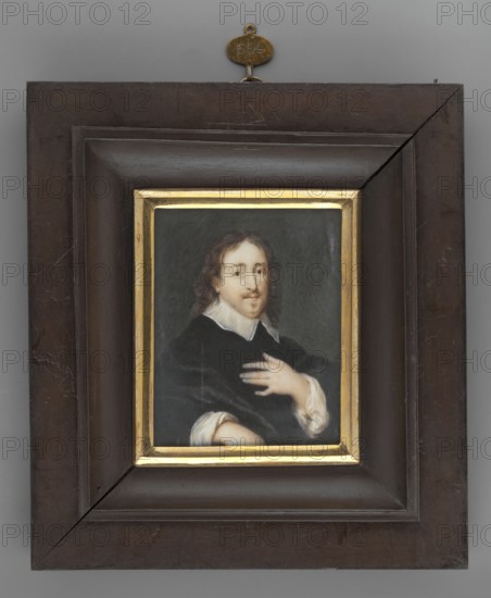 Portrait of a Man, Thil, Wilhelimine Louise du 1782–1819 painter; male portrait half-length; scholar/poet possibly; copy after a foreign miniature; repossession/provenance noted Jelenia Góra; miniature; 1820; 7.9 cm × 6.3 cm., A framed portrait of a person with pale skin and shoulder-length brown hair wearing a dark garment with a white collar and white sleeve cuffs, set against a dark gray-green background; the person has a mustache and goatee and holds a hand against their chest. The painting is surrounded by a thin gold inner frame and a wide dark brown wooden outer frame with visible scratches and a small metal hanging piece at the top in a brass color. The visible colors include dark brown, gold, black, white, pale skin tones, brown, gray, and brass.