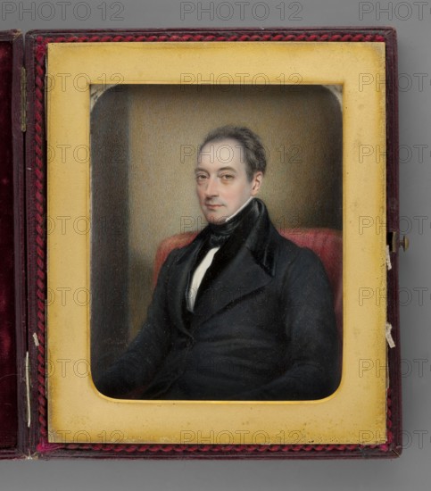 Portrait of a Man in a Frock Coat, painted by Henry Collen 1800–fl.1872, 1837. Seated waist-high, three-quarter left. Dark salt-and-pepper hair, hazel eyes. Wearing a white shirt, tie, vest, and black frock coat. Background shows the back of an armchair with red upholstery and a yellow-brown-gray wall. Miniature on cardboard, height 12.1 cm, width 9.7 cm. Binding: cherry leather case, metal frame with braided border, passe-partout. Inscribed bottom left: “H. Collen / 1837.” On the reverse in ink: “1837 / Painted by Henry Collen / miniature painter to / the Queen / and HRH The Duchess of Kent / 37 Somerset Street / Portman Square / London.” Pencil inscription on the cardboard edge: “Col Porter Cate / XII, 1837.”, A painted portrait of a seated man displayed inside a rectangular frame and a hinged case; the man wears a dark coat with a high collar and a white shirt visible at the neck, and he has short dark hair and a neutral expression. The frame around the portrait is a yellowish-cream...