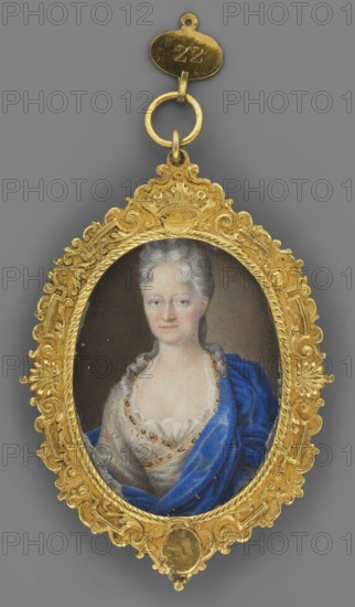 Sophie Louise von Hessen-Darmstadt 1670–1758, daughter of Louis VI, wife of Duke Albrecht Ernest zu Oettingen-Oettingen. Portrait by Franz Lippold 1688–1768. Half-figure, 3/4 left miniature, 1717, Germany. Silver-grey wig, blue eyes, white dress with a gold pattern trimmed at the neckline with a gold ribbon set with sapphires; sapphire coat. Gray-brown background, lightened on the right. Miniature height 6.0 cm, width 4.5 cm. Binding: richly ornamented gilded bronze., An oval miniature portrait set in an ornate gold frame suspended from a small gold loop, showing a woman with pale skin and powdered gray hair styled back with curls, wearing a low-cut pale dress with lace trim and a draped rich blue fabric over one shoulder; the frame is highly decorative with scrolling and floral motifs in gold, and the background behind the figure is a muted dark color.