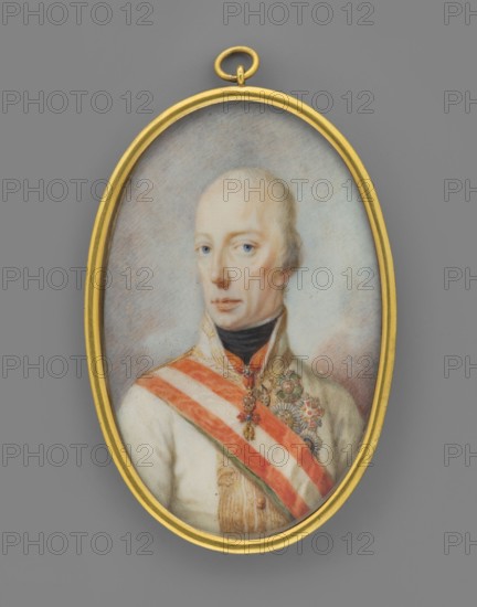 Francis II Habsburg 1768–1835, Emperor of Austria; unknown artist; male portrait miniature, ca. 1815; depicts ruler in uniform with orders; watercolor miniature, 6.1 cm × 3.8 cm; Austria; inscriptions/notes: men, rulers, uniforms, orders, portraits, foreign miniatures, politicians; provenance notes:, repossession Jelenia Góra, repossession Salzburg., An oval portrait miniature set in a gold frame shows a pale-skinned person with light hair and light-colored eyes, wearing a high-collared garment and a dark neck covering; a sash with alternating light and reddish stripes crosses the chest, and a few ornate medals or brooches with metallic and colorful details are pinned near the shoulder. The background is a soft blend of muted grays and pale blues, and the outer area surrounding the frame is a medium gray. The visible colors include gold, pale skin tones, light hair, light blue, dark black, reddish orange, white, greenish accents, and muted gray.
