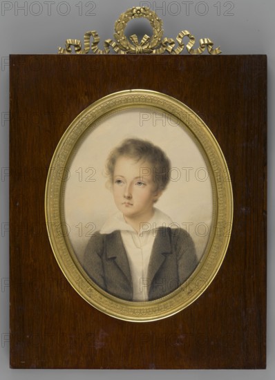 Portrait of Count Artur Sobanski 1814–1831, son of Izydor and Seweryna Potocka. Painter: Johann Nepomuk Ender 1793–1854. Boy, torso, shoulders straight, head three-quarters to the left. Wavy flaxen hair; regular facial features. Dark brown jacket, white vest and shirt with a turn-down collar. Background greyish-blue, uneven. Miniature, 1840, Vienna. Height 19.8 cm, width 15.3 cm., A framed oval portrait of a young person with light skin and light brown curly hair set against a pale background, shown from the chest up and wearing a dark jacket over a light collar; the portrait is surrounded by a decorative gold oval frame mounted on a dark brown wooden plaque topped with a gold decorative wreath and ribbon element; visible colors include shades of brown, gold, pale beige, light pink, gray, and white.
