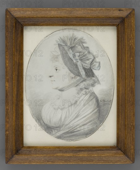 Portrait of an Elderly Woman Wearing a Hat in Profile, Taubert, Gustav Friedrich Amalius 1755-1839 painter. Women older, hats, headgear, profile left, female portrait, foreign miniature. Torso of an elderly woman in left profile. Hair in small curls revealing the forehead and falling to the shoulders. The hat is trimmed with a pale blue ribbon tied under the chin. The dress is high-waisted; the oval neckline is decorated with a ruffle, and a shawl with a faint bluish shadow is worn on the shoulders. Background: natural color of the paper. Binding: secondary, contemporary, wooden, 1797, Gdansk. Miniature, height 8.7 cm, width 6.9 cm., A framed oval portrait drawing of a woman shown in profile facing left, rendered in shades of gray and black on a light background; she wears a bonnet with ribbons and feather-like decoration, curly hair visible at the nape, a high neckline with ruffled trim, and a draped garment, all depicted with delicate pencil or charcoal shading; the frame is wooden w...