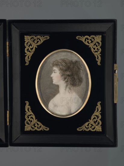 Profile portrait of Julia, née Princess Lubomirska, Countess Potocka; creator, profile female portrait showing hairstyle; miniature height 7.3 cm, width 5.8 cm; dated 1780; Poland Krzeszowice, Lesser Poland Voivodeship; Polish miniature; references Potocki, Andrzej Stefan; repossession provenance., A framed oval portrait of a woman in profile is set within a rectangular black frame decorated with ornate corner motifs; the portrait shows a pale-skinned woman with curly brown hair pulled back, wearing a light-colored garment, and the oval is bordered by a thin metallic ring. The black frame features golden decorative flourishes in each corner and a hinge and clasp in metallic tones at the side, and the background surrounding the frame is a muted gray.