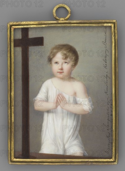 Mieczyslaw Sanguszko-Kowelski 1807-1813 as a child praying before a crucifix, painted by Anton Richter 1783-1850. Half-length, almost en face; blond hair, white shirt falling from the shoulders, hands folded in prayer. A crucifix on the left. Background gray, lightened around the figure. Frame: convex bronze bar. 1813. Miniature; height 9.3 cm, width 7.1 cm., A rectangular framed pendant with a gold-colored border contains a painted portrait of a young child with light brown curly hair and fair skin, wearing a white draped garment that exposes one shoulder and has hands clasped in front in a praying gesture; the child looks slightly upward with a neutral expression. To the left of the child is a dark brown wooden cross that extends vertically and horizontally. The background is a soft gray with subtle tonal variations, and the frame has a small round gold-colored loop at the top. Colors visible include gold, light brown, fair skin tones, white, dark brown, and gray.