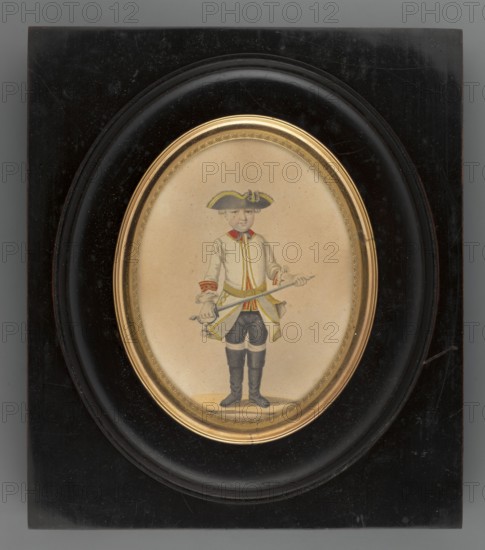 Prince of Hesse, Christian of Hessen-Darmstadt 1763–1830. Portrait of a boy, standing, full-length. He wears a white wig, grey-blue eyes, a black tricorn hat with yellow rim, a black bow under the neck, a white frock coat with red collar and cuffs with yellow piping and a yellow belt, a similar vest, black trousers and shoes, white gloves, and carries a silver saber. Style: foreign miniature. Frame: narrow oval gilt bronze rim with a palmette motif set in a wooden frame polished to look like ebony. Date: 1850. Medium: miniature. Dimensions: height 10.8 cm, width 8.3 cm. Creator: unknown., A framed oval miniature shows a full-length portrait of a young person standing and facing forward, wearing a tricorn hat with yellow trim, a light-colored coat with yellow and red trim, dark knee-length breeches, and tall dark boots; they hold a long thin object across their body and have a small pouch or ornament at their waist. The miniature is set on a beige background and surrounded by a decorati...
