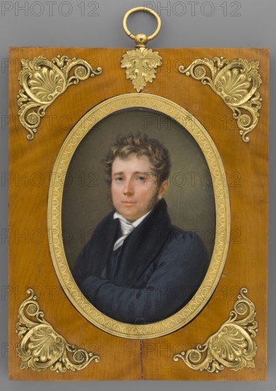 Artur Stanislaw Potocki from Krzeszowice 1787–1832; painter: Józef Bel Arthur Sonntag 1784–1834. Miniature portrait in Biedermeier style, en three-quarters, depicting a male aristocrat in period costume related to the Napoleonic campaign 1795–1815. Inscription/notes: Potocki. Dated 1828. Miniature, height 13.5 cm, width 9.6 cm., The image shows a framed oval portrait of a man with light skin and short curly brown hair wearing a dark blue coat and a white collar, set against a muted grayish background; the portrait is surrounded by an ornate gold oval frame mounted on a warm brown wooden rectangular panel decorated with decorative gold corner embellishments and a gold hanging ring at the top; visible colors include brown, gold, dark blue, white, gray, beige, and flesh tones.
