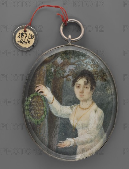 Portrait of Barbara Dabrowska, née Chlapowska 1782–1848, second wife from 1807 of General Jan Henryk Dabrowski; miniature portrait by M. Feist ca. fl. 1800–1820, amateur painter. Oil/miniature, 1810. Subject: Barbara Florentyna Chlapowska—accompanied her husband during Napoleon's expedition to Russia and transported his wounded husband to Vilnius; mentioned in the fourth verse of the Polish national anthem Listen, Basia.... Inscription inside binding: M. Feist made. Inscription inside wreath of oak leaves: Dedie/Au jour/le plus cheri/28 Aout/1810. Dimensions: height 6.2 cm, width 5.1 cm. Depicted: woman in three-quarters, wearing jewellery and a wreath, set against a park/landscape with plants and trees; empire style., An oval pendant with a metal rim and ring at the top contains a painted miniature of a woman in a white dress standing before a tree and foliage; she has dark curled hair and a pale complexion, and she wears gold-colored jewelry including a necklace and bracelets, while ...