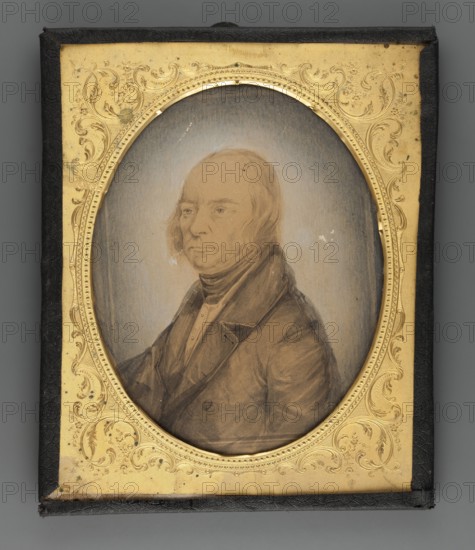 Cyprian Szukiewicz ca. 1775–1844, godfather of Cyprian Kamil Norwid; painter; portrait in three-quarters of a man; male portrait; Polish miniature; amateur artist; ; subject: man of letters; dated 1860; place of creation: Poland; miniature; 11.5 × 9 cm., An oval portrait of an older person with light skin tones and pale hair is set within an ornate rectangular frame; the person wears a dark coat and a high collar with layered garments visible, and their expression is neutral. The portrait background is a muted grayish-blue gradient. The frame surrounding the oval is gold with intricate floral and scroll embossing, and the outer border of the rectangular case is black. Overall visible colors include pale skin tones, light beige, grayish-blue, brown, gold, black, and muted dark brown.