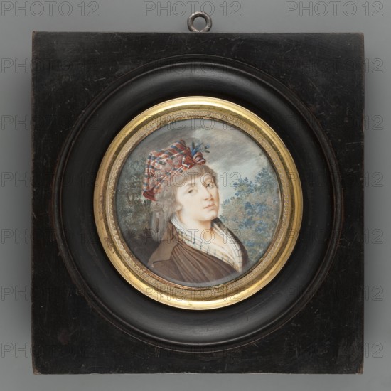Portrait of a woman in a stylised Krakus cap. Miniature portrait en trois-quarts, bust 3/4 right, ash-grey hair; on the head a scarf with blue, white and red stripes tied in the form of a rogatywka; at the bodice a white scarf with blue stripes; brown dress. Background: thicket, trees and sky with dark clouds. Frame: a circular rim of gilded bronze in a circular recess in a square wooden frame polished to ebony. The portrait may be an allusion to the Kosciuszko Uprising; peasant women wore scarves on their heads, and brown was particularly associated with the Third Estate. Attributed to unknown artist; ca. 1830. Miniature, height 6.4 cm, width 6.5 cm., A round portrait set in a circular gold frame mounted on a square black wooden plaque shows a person with light skin and light-colored hair wearing a patterned red and blue head covering and a brown garment with a white collar; the background contains foliage in green and blue tones against a grayish sky, and the frame and plaque display...