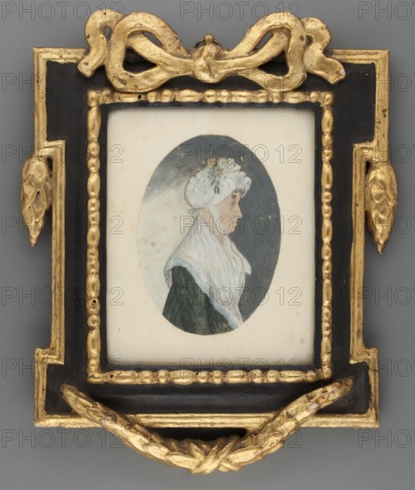 Portrait of an Elderly Woman in Profile, pendant to Min.745, costumes, women, headgear, dresses, profiles portraits, Polish miniatures, amateurs, unknown origin provenance, after 1800, miniature, height 9.0 cm, width 6.4 cm, A small oval portrait of a person in profile is set within a rectangular mat and an ornate frame; the portrait shows a figure wearing a white lace cap with small floral decoration and a white shawl over a dark green garment against a muted gray-blue oval background, rendered on a cream-colored mount. The surrounding frame is rectangular with a black inner field and gilded molded ornamentation, including a decorative bow-like motif at the top, foliate elements at the sides, beaded inner edging, and a knotted ribbon-like ornament at the bottom; visible colors include white, dark green, gray-blue, cream, black, and gold.