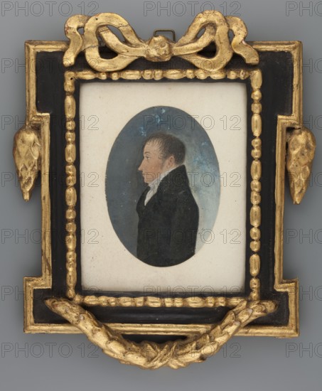 Portrait of a man in profile, pendant to Min.744, unknown creator amateur painter, male portrait in profile, Polish miniature, after 1800, watercolor miniature, height 9.0 cm, width 6.5 cm, A small framed portrait shows a side-profile of a man inside an oval painted area; the man wears a dark coat and a white collar and has short brown hair and a pale skin tone. The oval background is bluish with lighter and darker blue areas. The surrounding mat is off-white. The frame is decorative with a combination of black and gold elements, including a gold ribbon-like ornament at the top, gold beaded inner border, gold leaf-like motifs at the sides, and a gold swag at the bottom. The overall color palette includes black, gold, blue, white, brown, gray, and pale skin tones.