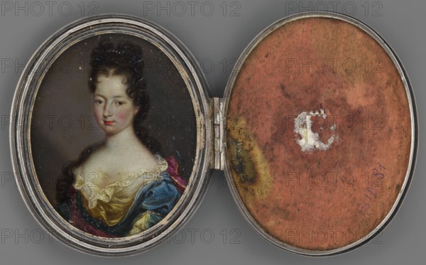 Portrait of a young woman, unknown artist, shoulder-length portrait of a young woman facing left, wearing a 17th/18th-century dress with hair pinned up high; foreign miniature; inscribed/provenance notes:, repossession Jelenia Góra; dated 1710–1720; miniature, height 6.3 cm, width 5.1 cm., An open oval locket with a metal rim shows a painted portrait of a woman on the left and a worn fabric lining on the right; the woman has pale skin, dark brown curled hair piled high with ringlets falling over her shoulders, a calm facial expression, and flushed cheeks with pink tones, wearing a low-cut dress with lace at the neckline and draped fabrics in blue, gold, and deep red, set against a dark background, while the opposite side displays a mottled worn fabric in shades of reddish-brown, burnt orange, and yellowed stains with a small area of white residue and a hint of purple marking, all contained within a silvery metal hinge and frame.