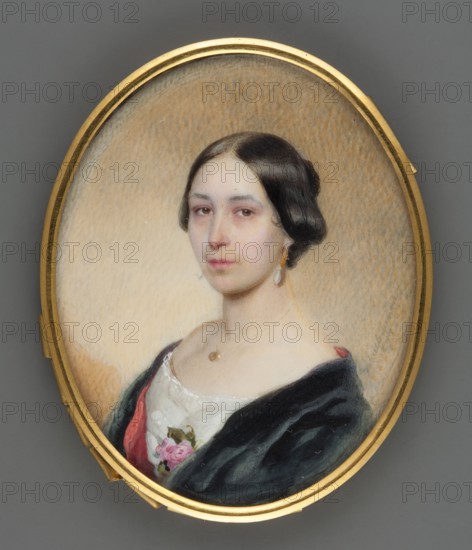 Portrait of a Woman, Decker, Gabriel 1821–1855 painter, shoulder-length portrait of a woman right, hairstyle: bun, foreign miniature, 1847, miniature, height 6.4 cm, width 5.1 cm, An oval portrait set in a gold frame shows a woman with pale skin and dark brown, center-parted hair styled close to her head; she gazes slightly to the viewer’s left with a neutral expression. She wears a dark outer garment with a velvety appearance over a white bodice that has lace trim and a pink floral decoration near the neckline. A teardrop-shaped earring hangs from one ear and a small pendant rests at her throat. The background within the frame is a warm beige with subtle textured shading, and the frame contrasts with the surrounding gray surface outside the oval.