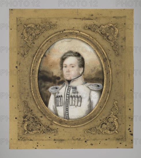 Second lieutenant of the First Krakus Regiment, unknown painter, 1831, Poland; miniature, height 10.3 cm, width 9.1 cm., A painted portrait of a young person shown from the chest up set inside an oval frame and mounted on a rectangular decorative backing; the person wears a white military-style coat with shoulder epaulettes and a high collar, has light skin and short wavy brown hair, and looks straight ahead with a neutral expression. The painted background behind the figure shows soft blended tones in muted brown and gray. The oval frame is gold with textured ridges, and the rectangular backing is a dull gold or yellowed beige with ornate floral corner decorations in a darker gold and scattered dark spots and speckles across its surface. The visible colors include white, gold, beige, brown, gray, black, and subtle flesh tones.