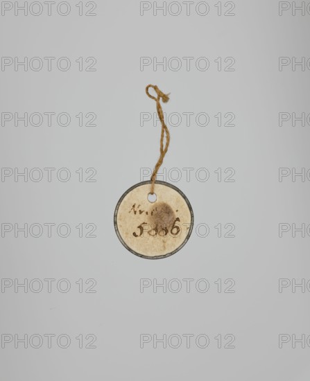 Captain of the 2nd Line Infantry Regiment, Kurowski, Józef Szymon 1809–1851 painter, 1831, miniature, height 5.2 cm, width 4.7 cm, A round, aged paper tag with a darker rim hangs from a twisted, frayed tan string; the tag shows discoloration and a circular stain and is set against a smooth light gray background with subtle variations in tone.