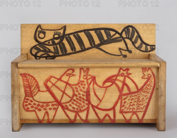 A wooden bench from a set of doll furniture. Wooden bench with a box closed by a flap forming a seat. Painted decoration with schematic animal silhouettes: a tabby cat on the backrest and chickens on the sides and front wall of the box. Toy, height 11.5 cm, width 17.0 cm, depth 8.0 cm. Maker: Kenar, Antoni 1906–1959, sculptor. Date: 1947–1948. Origin: Zakopane. Associated with State Secondary School of Fine Arts in Zakopane and Office of Production Aesthetics Supervision 1947–1949., A small wooden box with a hinged back shows a simple black line drawing of a reclining striped cat on the back panel and a group of stylized birds drawn in red across the front panel; the wood is a warm tan color with visible grain, the cat features bold black stripes and round eyes, and the birds are outlined and patterned with red marks.