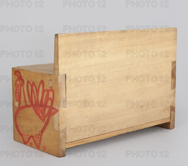 Wooden bench from a set of doll furniture. Wooden bench with a box closed by a flap forming a seat. Painted decoration with schematic animal silhouettes — a tabby cat on the backrest and chickens on the sides and front wall of the box. Toy, height 11.5 cm, width 17.0 cm, depth 8.0 cm. Made 1947–1948, Zakopane. Maker/creator: Kenar, Antoni 1906–1959; designed at the State Secondary School of Fine Arts in Zakopane and produced by the Office of Production Aesthetics Supervision 1947–1949., A rectangular wooden box with a pale beige wood grain finish sits against a light gray background, showing a taller back panel and shorter front with visible joinery at the corners; one side panel features a red hand-drawn stylized bird or rooster-like figure and some decorative red markings, and the wood shows natural variations in light brown and tan tones with some darker brown edges and small scuff marks.