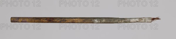 Jan Stanislawski's flat brush; Jan Stanislawski 1860–1907, painter; painting accessory brush used for plein-air painting; late 19th century; height 13.5 cm, width 0.6 cm; varia., A long cylindrical object lies horizontally against a plain light gray background; the object appears worn and textured with a mix of colors including brown, tan, muted green, white, purple, blue, and rust tones, and one end shows frayed thin strands protruding while the opposite end is blunt and slightly darker.