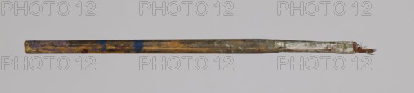 Jan Stanislawski's flat brush; Jan Stanislawski 1860–1907, painter; painting accessory — flat brush used for plein-air painting; late 19th century; dimensions: height 13.5 cm, width 0.6 cm; varia., A horizontal slender rod with a worn wooden shaft showing a mix of brown, yellow, and ochre tones with patches of blue and purple paint, transitioning toward a metallic-looking section near one end that is silvery and gray with some greenish and reddish spots, and frayed brown fibers protruding from the tip; the background is a pale gray.