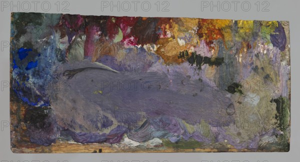 Jan Stanislawski's rectangular palette; Jan Stanislawski 1860–1907, painter; painting accessory — painter's palette; associated with plein-air painting and painter's workshop; late 19th century; varia; height 7.5 cm, width 14.4 cm, A rectangular surface covered in thick layered paint showing a large central area of muted purple and gray brushstrokes, surrounded by patches of vivid blue on the left, deep red and magenta near the top, warm yellow and orange toward the upper right, and areas of green and olive along the right edge and bottom; there are also creamy beige and off-white smudges, small dark black and charcoal spots, and a worn wooden strip visible along the bottom edge.