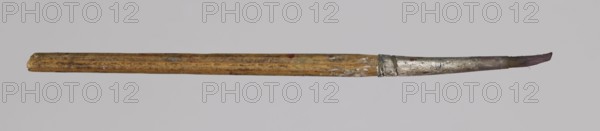 Jan Stanislawski's round brush; Jan Stanislawski 1860–1907 painter; painting accessory brush used for plein-air painting; late 19th century; height 13.5 cm, width 0.7 cm; varia., A single, slender paintbrush lies horizontally against a pale gray background, showing a worn wooden handle with a faded yellowish-brown color and patches of darker brown and small specks of paint, a metal ferrule with a tarnished silver-gray appearance and areas of darker discoloration, and a narrow brush tip with bristles that appear stained in reddish-brown and dark brown tones.