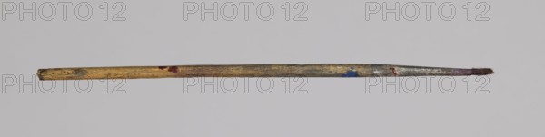 Jan Stanislawski's round brush; Jan Stanislawski 1860–1907 painter; painting accessory brush used for plein-air painting; late 19th century; dimensions: height 13 cm, width 0.4 cm., A single long thin object resembling a worn paintbrush with a wooden handle showing shades of tan, brown, and gray, small areas of red and blue paint on the handle, a metal ferrule with patches of silver and dark discoloration, and a frayed brush tip with dark brown bristles against a pale gray background.