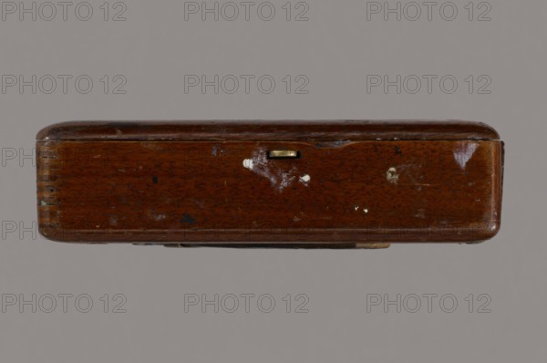 Jan Stanislawski's painting box; painter Jan Stanislawski 1860–1907; painting implements; artists in the open air; painting accessories; plein air studies; late 19th century; varia; height 10 cm, width 16 cm, depth 3.5 cm, A rectangular wooden box viewed from its long side with rounded corners and a glossy finish showing scratches and worn areas, a small metallic rectangular latch inset near the top center, a few small spots of chipped paint and scuffs across the surface, and a plain neutral background. The visible colors include brown on the wood, gold on the latch, white from the chipped spots, and a gray background.