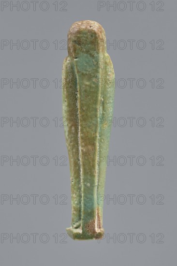 Ankhren's shabti, Ankh-ren name. Mummy-shaped figurine, funerary shabti, standing on a base and supported at the back by a pilaster. Arms crossed on the chest, holding hoes in both hands; a string in the right hand suspends a basket over the left shoulder. Convex tools. Smooth, three-part wig with ears uncovered. Facial details slightly blurred, large eyes, proportionate nose, straight long beard. Inscription engraved in a column on the front of the legs: The word spoken by Osiris Ankh-ren .... Date: 664–30 BC Late Period–Ptolemaic Period. Provenance: Tuna el-Gebel. Height: 10.8 cm., A vertical elongated figurine-like object with a rounded top and tapered bottom, shown against a plain gray background; the surface of the object displays a mix of green and turquoise hues with areas of brownish tan and pale beige patina, a textured and slightly worn finish with visible small pits and rough spots, and subtle linear ridges running vertically along its length creating narrow recessed panels ...