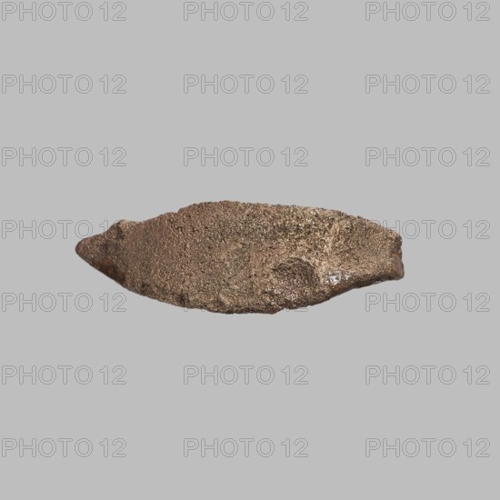 Eye setting, Small eye setting, from a child's sarcophagus mask or from a figurine's face; boat-shaped. Sarcophagus fragments; eyes, masks, faces. ca. 1550–332 BC, New Kingdom–Late Period, Egypt. Sarcophagus mask, sculpture, height 3 cm., A roughly elongated, irregular object with a textured, granular surface in shades of brown and bronze sits against a flat light gray background, showing uneven edges and a slightly pointed tip on one end and a thicker rounded end on the other, with subtle highlights and darker brown crevices across its surface.