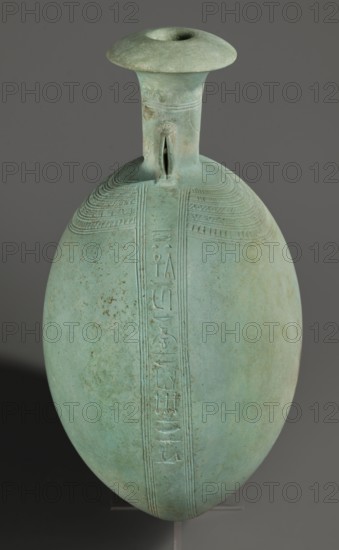 New Year's canteen, Goluchów Greater Poland Voivodeship. Flat round faience canteen with a narrow short neck ending in a chipped spout shaped like a papyrus capital. Decorated on both sides with plastic figurines of crouching baboons, elbows on knees and paws supporting the muzzle. A floral necklace is depicted in relief on both sides of the neck, and a hieroglyphic text runs along the narrow sides. Egyptian, Late Period, 26th Dynasty, 664–525 BC. Vessel; height 17.5 cm plus 1.5 cm base, width 13.7 cm, weight 0.37 kg., A single elongated rounded vessel with a narrow cylindrical neck and flaring rim sits against a neutral gray background; the vessel is predominantly light green with areas of pale turquoise and subtle brown spotting, and it features incised linear decorative bands and a vertical relief strip running down its front, with a small looped handle where the neck meets the shoulder.
