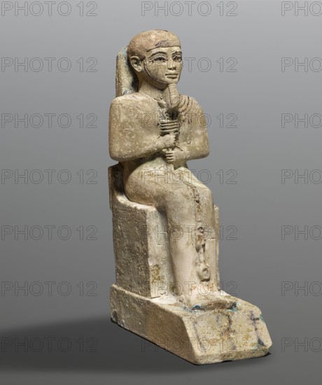 Figurine of the god Ptah. Figurine of the god Ptah sitting on a throne, on a base in the shape of the sign of Maat. He holds a composite scepter in his hands. Materials and type: figurine; back pillars, hieroglyphs, scepters, thrones, ankh, uas, djed pillars. Subject: Ptah Egyptian deity. Maker: unknown. Date/place: c. 1550–c. 1295 BC; New Kingdom, 18th Dynasty, Egypt. Dimensions: height 29 cm, width 10.5 cm, depth 19 cm; weight 2.736 kg., A seated carved figure rendered in a weathered beige stone with traces of pale blue and darker brown patina, shown against a neutral gray background; the figure wears a close-fitting head covering and a long backpiece, has stylized facial features with darkened eye accents, and holds a vertical object with both hands at chest level; the body and clothing show surface wear and slight color variations from beige to off-white with areas of darker brown staining, and the base on which the figure sits has chipped edges and faint blue-green discoloration.