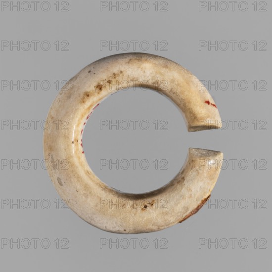 Ring - hair ornament, Goluchów Greater Poland Voivodeship, rings, hair ornaments, ca. 1550–1069 BC; New Kingdom, Egypt; jewelry; diameter 3 cm, A round, open circular object with a gap, shown against a plain gray background; the object has an off-white to beige surface with areas of darker brown discoloration and small speckles, a few reddish spots on the inner curve and near one outer edge, and a slightly glossy, worn texture with smooth, rounded edges.