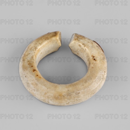Ring — hair ornament;, From Goluchów Greater Poland Voivodeship. Rings, hair ornaments; New Kingdom, Egypt, ca. 1550–1069 BCE. Jewelry; diameter 3 cm., A roughly circular, open ring-shaped object with a smooth, rounded surface and two flat, squared-off ends, showing a mottled beige and off-white color with a few darker brown spots and patches, placed on a light gray background.