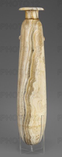 Alabastron, Slender alabastron with a distinct short cylindrical neck and a wide flat rim, provided with two tiny handles in the form of suppositories. Stone vessel for oils and ointments. Height 32 cm + 1.5 cm base, width 5 cm, weight 1.11 kg. Date: 664–332 BC, Late Period, Egypt., A tall, elongated stone object with a rounded top and narrow base displayed upright on a clear stand; the surface shows layered, wavy banding in shades of cream, beige, tan, light brown, and off-white, with subtle darker streaks and small speckled spots; the object has a smooth, polished appearance and a small, slightly flared cap at the top with visible joins and color variations; the background is a solid neutral gray.