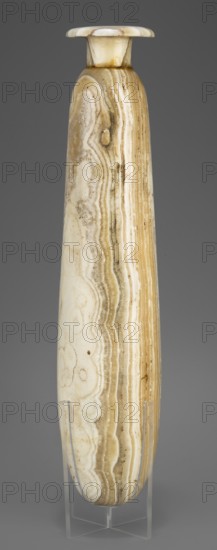 Alabastron, Slender alabastron with a distinct short cylindrical neck and a wide flat rim, provided with two tiny handles in the form of suppositories; stone vessel for oils and ointments, Egyptian art, Late Period, 664–332 BC; vessel alabastron, height 32 cm +1.5 cm base, width 5 cm, weight 1.11 kg, A tall, narrow, cylindrical vessel with a flared rim displayed upright on a clear stand, showing layered banding and swirling patterns in shades of beige, cream, tan, and light brown, with subtle darker brown streaks and small spots; the surface appears smooth and polished with natural banded striations running vertically along the body and concentric swirls visible in places, set against a plain gray background.