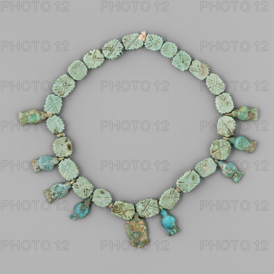 Necklace of amulets and beads; Cornflowers, face of Hathor, and flat fluted plates with crosses. ca. 1550–1295 BC; New Kingdom, 18th Dynasty, Egypt. Amulet/jewelry; height 30 cm., A circular arrangement of small round and irregularly shaped beads forming a necklace on a neutral gray background, with most beads in shades of pale green and turquoise and a few showing darker teal and brownish corrosion; several round beads have scalloped edges and shallow incised patterns, and a few pendant-shaped beads hang from the lower arc with varied weathered surfaces and mottled blue-green and brown coloration.