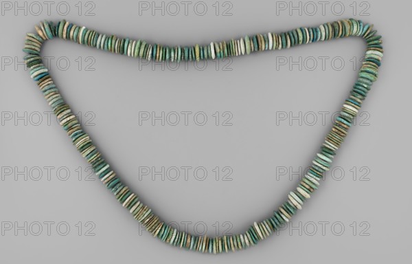 Necklace of disc-shaped beads. Long necklace consisting of flat, disc-shaped beads thicker in the middle than at the edge. Faience: white, green, blue. ca. 1550–1295 BC; New Kingdom, 18th Dynasty, Egypt. Jewelry; bead. Height 72 cm., Place of origin: Goluchów Greater Poland Voivodeship., A necklace made of a long strand of flat, disc-like beads arranged closely together, forming a loose triangular loop against a plain light gray background; the beads vary slightly in thickness and surface texture and display a range of colors including shades of green, turquoise, teal, blue-green, pale green, and hints of beige and brown, with some beads appearing more weathered or patinated than others.