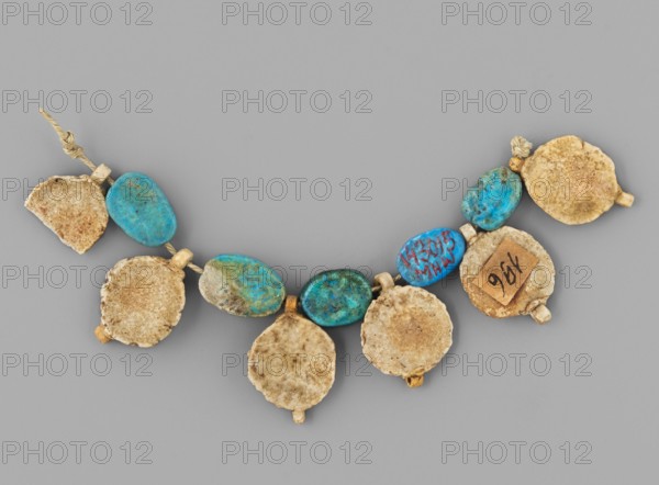 Fragment of a necklace — rosettes and flat beads; maker, found in Goluchów Greater Poland Voivodeship; rosettes, necklaces, beads, grave goods; 6 white rosettes with a yellow center and 5 blue beads; ca. 1550–1295 BC, New Kingdom, 18th Dynasty, Egypt; amulet jewelry., A curved string of beads laid on a neutral gray background, consisting of a mix of oval turquoise beads showing mottled blue and green tones and flat round beads with a rough, sandy beige surface; the beads are tied together with a natural-colored twisted cord and small beige spacer beads, and there is variation in texture with some beads appearing smoother and some more weathered.