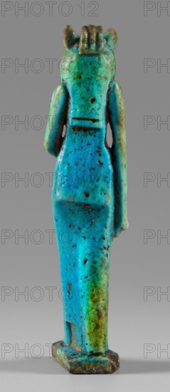 Amulet - figurine of a lion-headed goddess. A lion-headed goddess, in a tripartite wig and a narrow robe, walks with a lotus scepter in her left hand the right one lowered. Presumably the goddess Sekhmet; may relate to Wadjit or Bastet. Grave good; Egyptian, Late Period, 664–332 BC. Material: amulet; height 8.8 cm, width 1.7 cm., A vertical turquoise and green small statuette of a standing human-like figure shown from the back against a gray background, with a smooth elongated body and visible arm shapes at the sides, a rectangular base at the feet, a rounded head with short ridged detail at the top and small ear-like protrusions, a speckled and pitted surface with darker brown spots and areas of weathering, and visible transitions between bright blue-green, teal, and patches of olive green and brown.