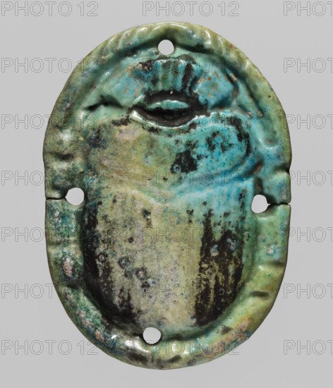 Scarab appliqué, scarab amulet made as an appliqué, likely part of a mummy net; grave goods, protective amulet, decorative element; Egypt; height 5.6 cm, width 4 cm., An oval, slightly irregular object with a raised central form resembling a beetle or scarab, showing a glazed surface in shades of turquoise, aqua, green, pale blue, and muted yellow-green, with areas of dark brown and black discoloration and spotting, a few small chips and worn patches on the edge, three round holes near the top, sides, and bottom, and a textured rim with dents and uneven glazing, all set against a plain light gray background.