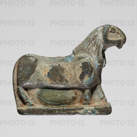 Amulet — ram; creator, Goluchów Greater Poland Voivodeship; ram, sacred animal; protective amulet; 664–332 BC, Late Period, Egypt; amulet; height 2.2 cm, width 0.7 cm, A small sculptural object shaped like a reclining animal with a stylized head and mane sits on a rectangular base; the surface shows a mottled patina with shades of blue, green, brown, tan, and gray, with areas of rough texture and smoother worn spots, and the form includes rounded body contours, a pronounced neck and head with carved grooves suggesting a mane, a curved tail at the rear, and short, sturdy legs connecting the body to the base.