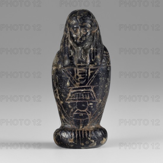 Amulet - god Osiris in hydria; maker, Osiris Canopic mythology; Egyptian deities; Egyptian religion; 1st–2nd century AD, Roman period, Egypt; amulet; height 4.9 cm, width 2.1 cm, A small carved figure standing upright on a rounded base, with a stylized human-like face and long hair or headdress that falls to the shoulders; the body tapers downward and is inscribed with linear carved motifs and geometric patterns. The surface shows worn areas and mottled spots, with visible scratches and chips. The dominant colors are dark black with lighter beige or tan wear marks and some gray tones in the background.