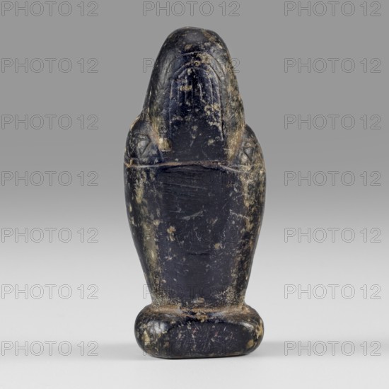 Amulet - god Osiris in hydria; Osiris canopic; Egyptian deities; Egyptian religion; 1st–2nd century AD, Roman period, Egypt; amulet; height 4.9 cm, width 2.1 cm, A small carved object shaped like a standing figure with a rounded head and broad shoulders, showing a smooth worn surface with chips and patches of abrasion. The piece appears primarily dark in color with areas of lighter discoloration and mottling, including beige and grayish tones where the surface is worn. The figure has shallow incised details on the head and shoulders and sits on a rounded base that shows similar wear and lighter spotting. The background is a smooth gradient ranging from mid gray at the top to pale gray at the bottom.